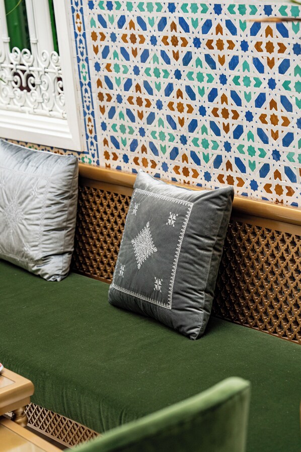 A green sofa with two pillows, one grey and one white, against a wall with a geometric tile pattern.