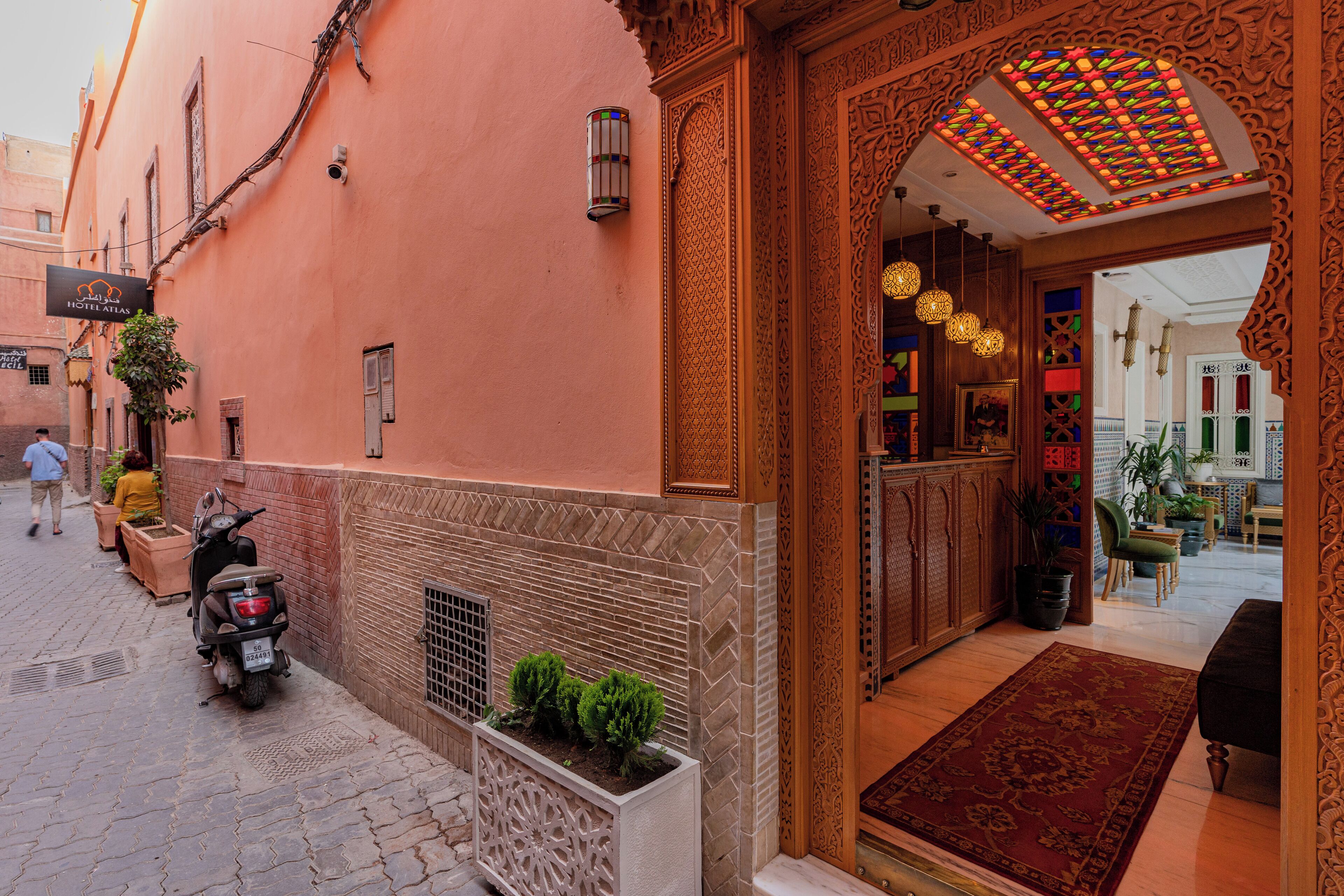 A hotel entrance with ornate architectural details, a potted plant, and a scooter parked outside.