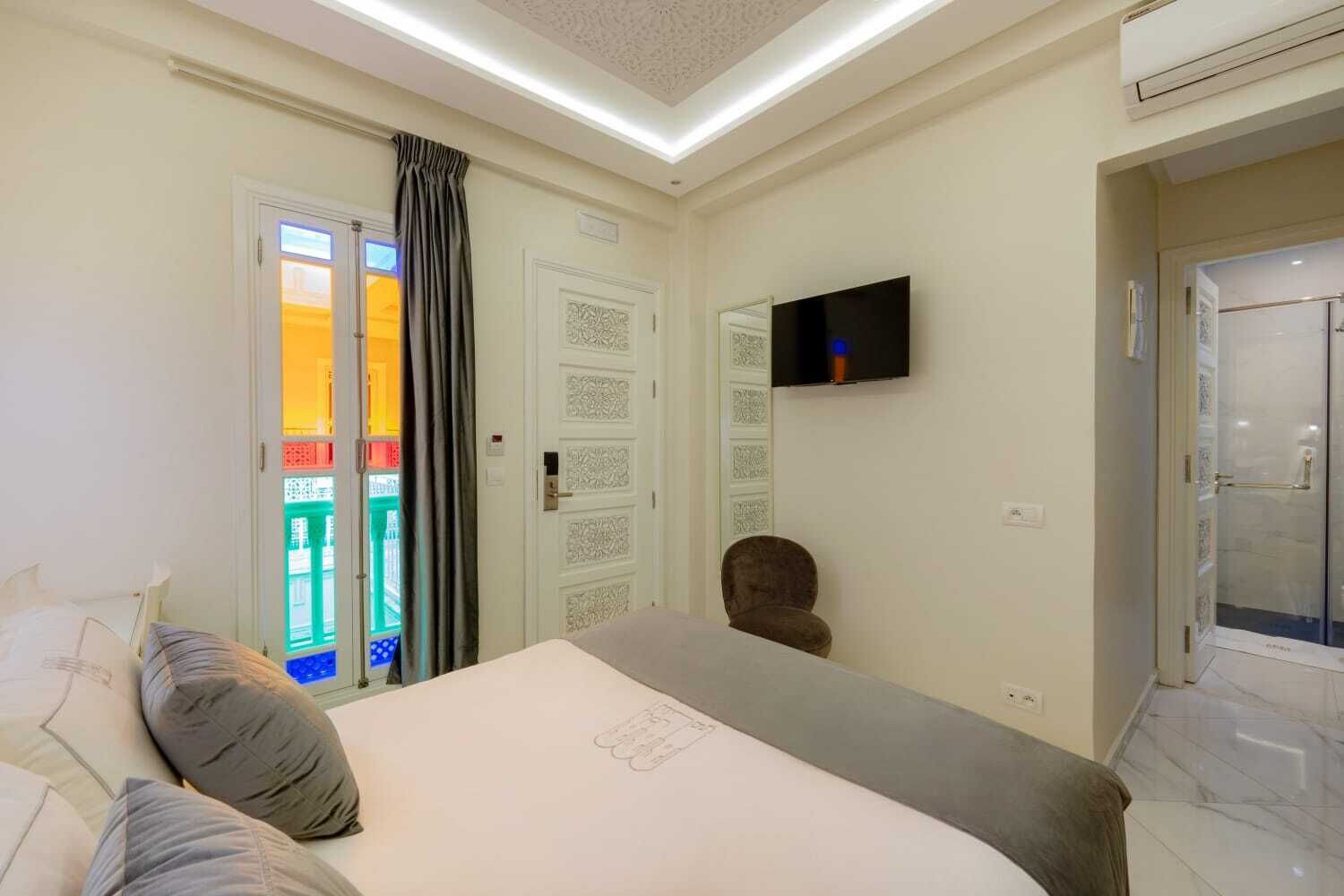 A hotel room with a bed, a TV mounted on the wall, a door with a frosted glass panel, and a shower area.