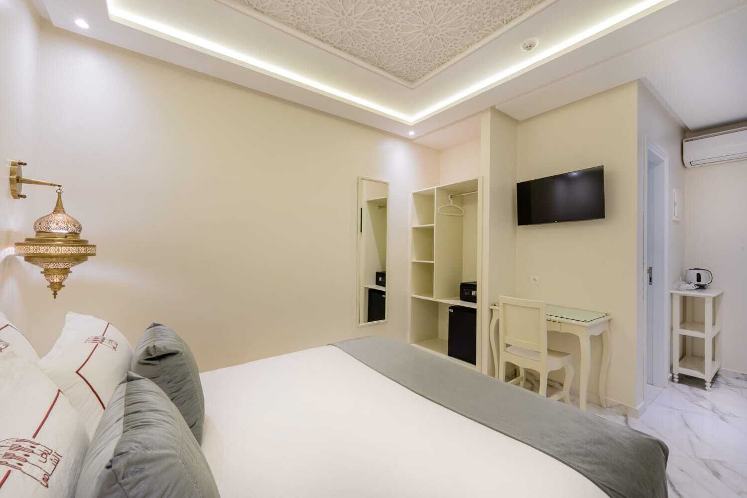 A bedroom with a bed, bedside table, TV, wardrobe, and a mirror.