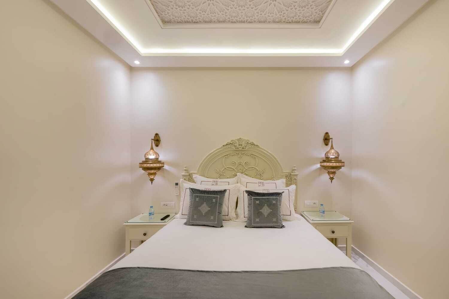 Une chambre bien rangée, avec un grand lit, deux tables de chevet et deux lampes fixées au mur.