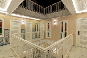 Interior com vários níveis, caracterizado por grades brancas ricamente decoradas, portas ornamentais e paredes com azulejos estampados.