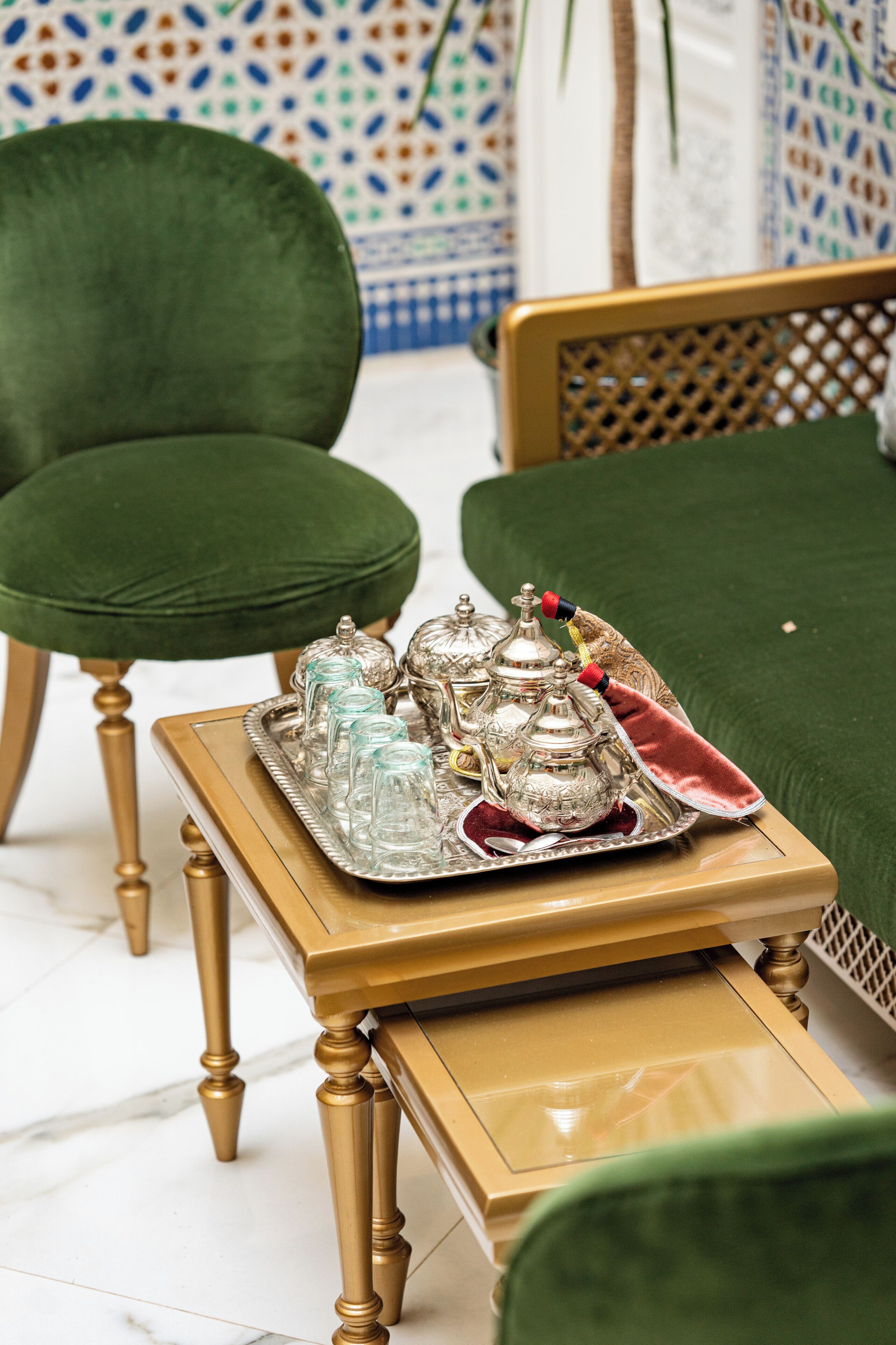 Une pièce comprenant un fauteuil recouvert d’un tissu vert, un canapé assorti de la même couleur, et un plateau avec de la verrerie et des théières en argent, le tout posé sur une table en bois.