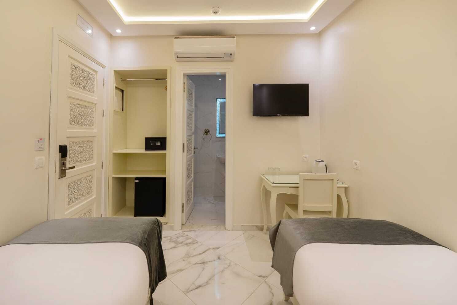Una habitación de hotel con dos camas, un escritorio, una silla, un televisor y un armario.