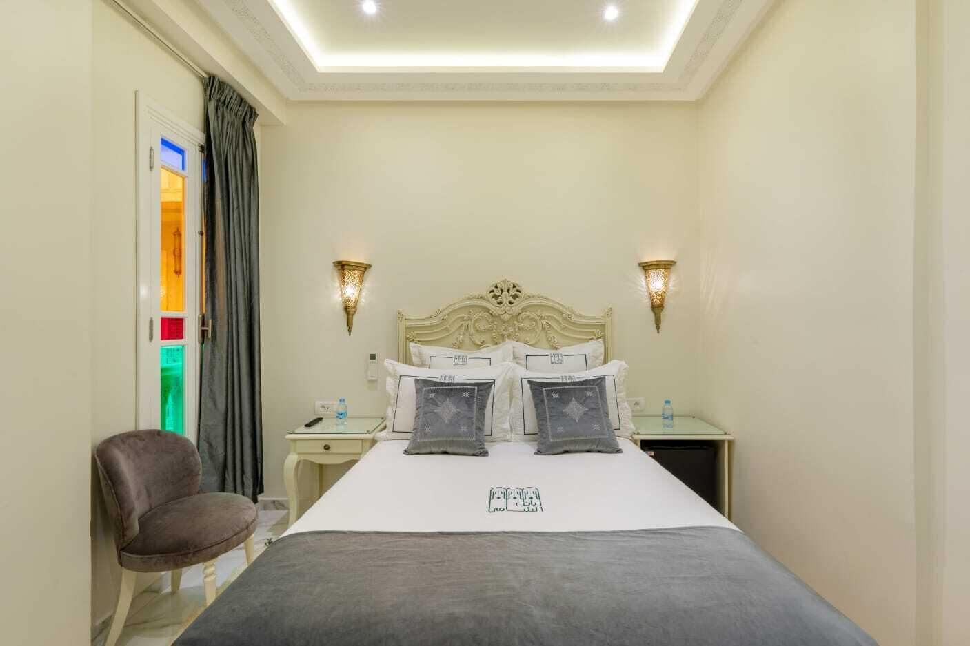 A hotel room with a bed, two bedside tables, a chair, and a wall-mounted light fixture.