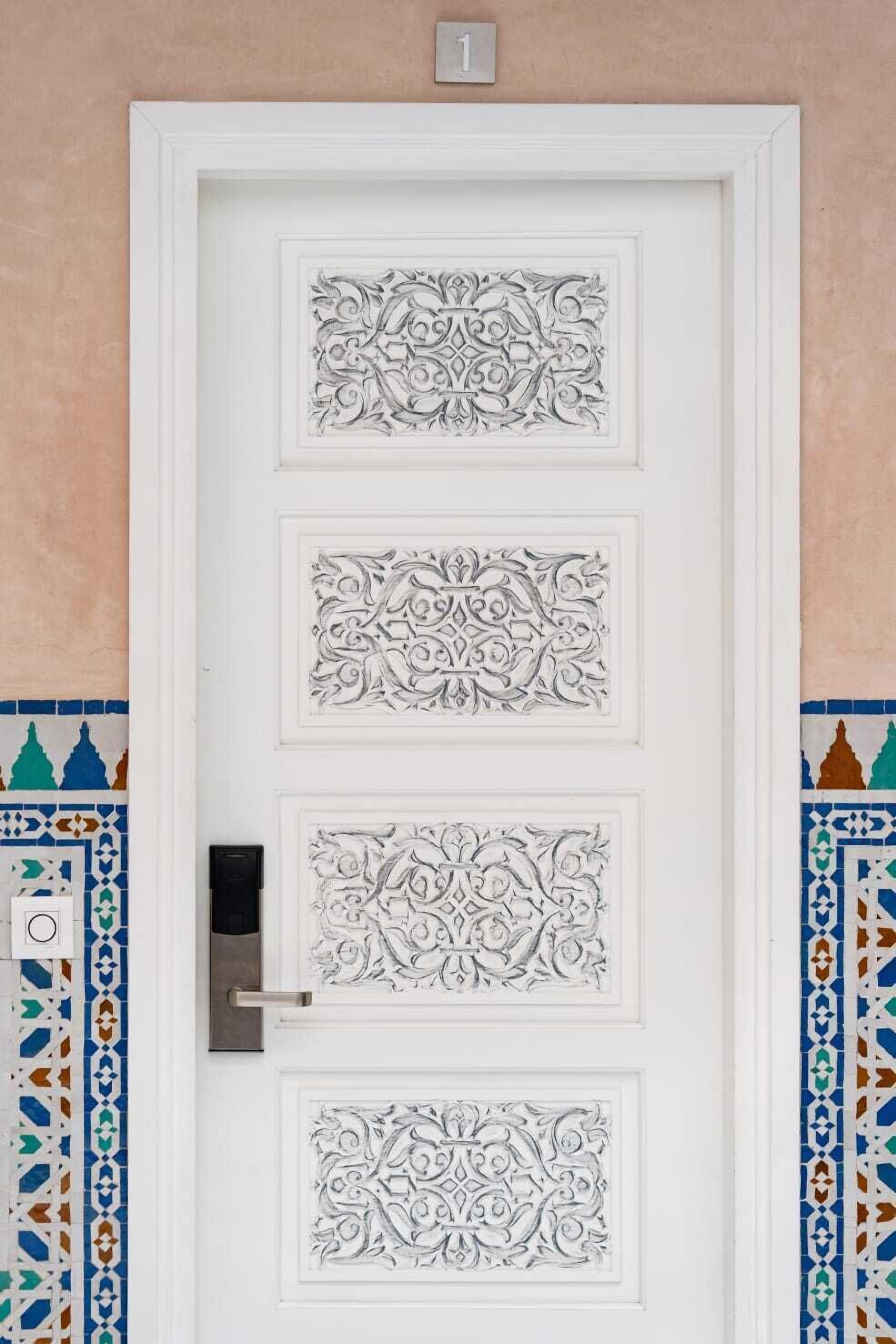A white door with intricate carvings and a numbered plaque above it.