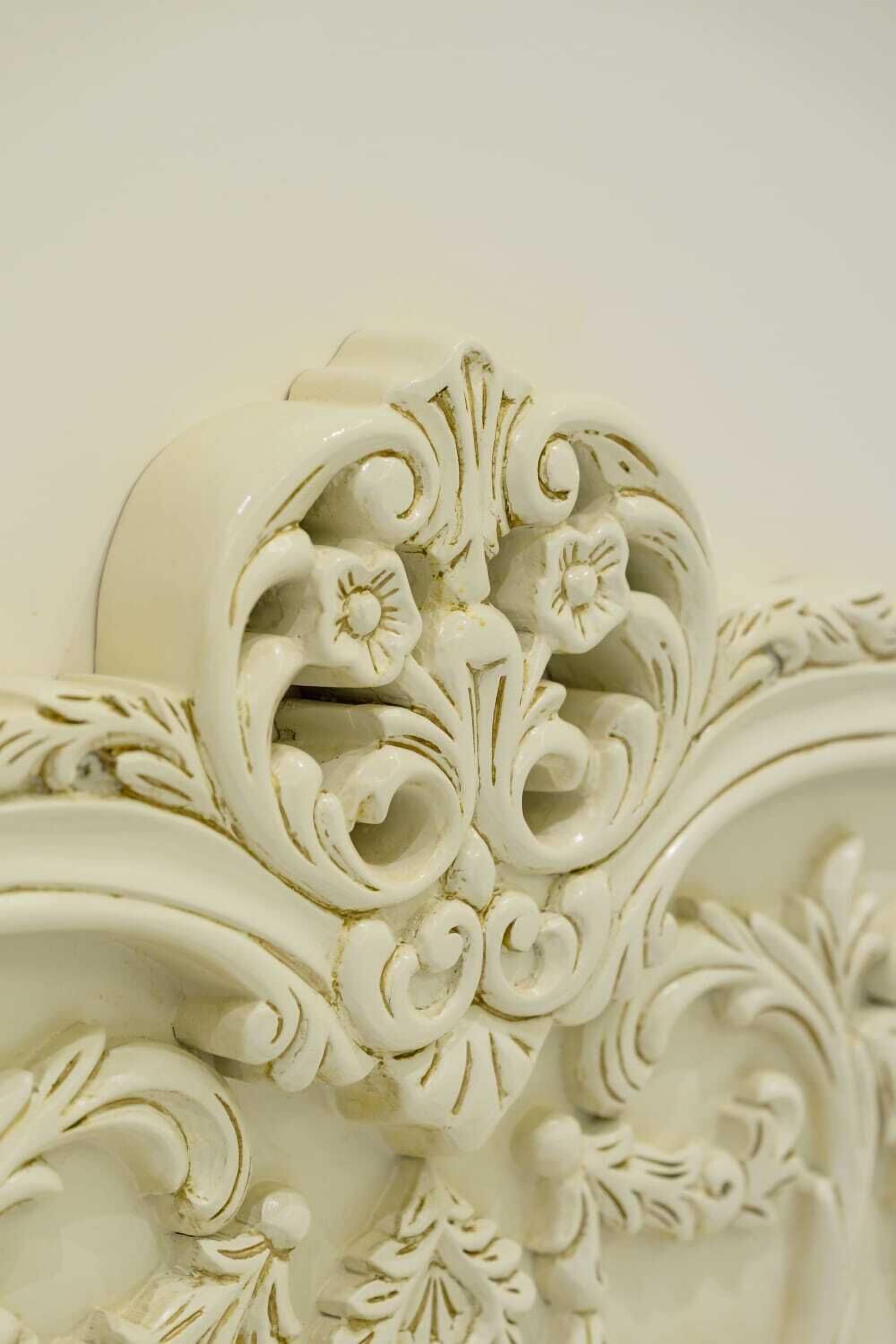 A close-up of ornate white wall molding with floral and scroll designs.