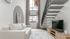 Uma sala de estar moderna com sofá, televisão, escada e janelas amplas.
