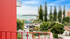 Varanda com guarda-corpo vermelho com vista para uma cidade costeira, com árvores altas e edifícios.