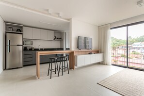Una cocina moderna con una isla central, taburetes de bar, un televisor de pantalla plana y un amplio ventanal con vistas a la ciudad.
