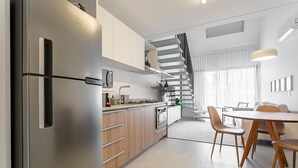 Uma cozinha moderna com geladeira de aço inoxidável, armários de madeira e um espaço de refeições com mesa redonda e cadeiras.