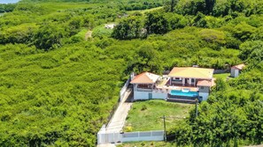 Situated amidst lush greenery, this property features a single-story building with a red-tiled roof and a swimming pool.