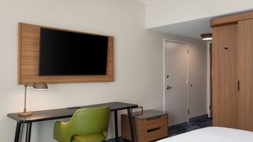 Une chambre d’hôtel comprenant un lit, un bureau avec une chaise, un téléviseur fixé au mur, une armoire et une porte.