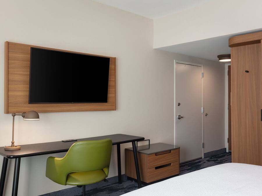 Une chambre d’hôtel comprenant un lit, un bureau avec une chaise, un téléviseur fixé au mur, une armoire et une porte.