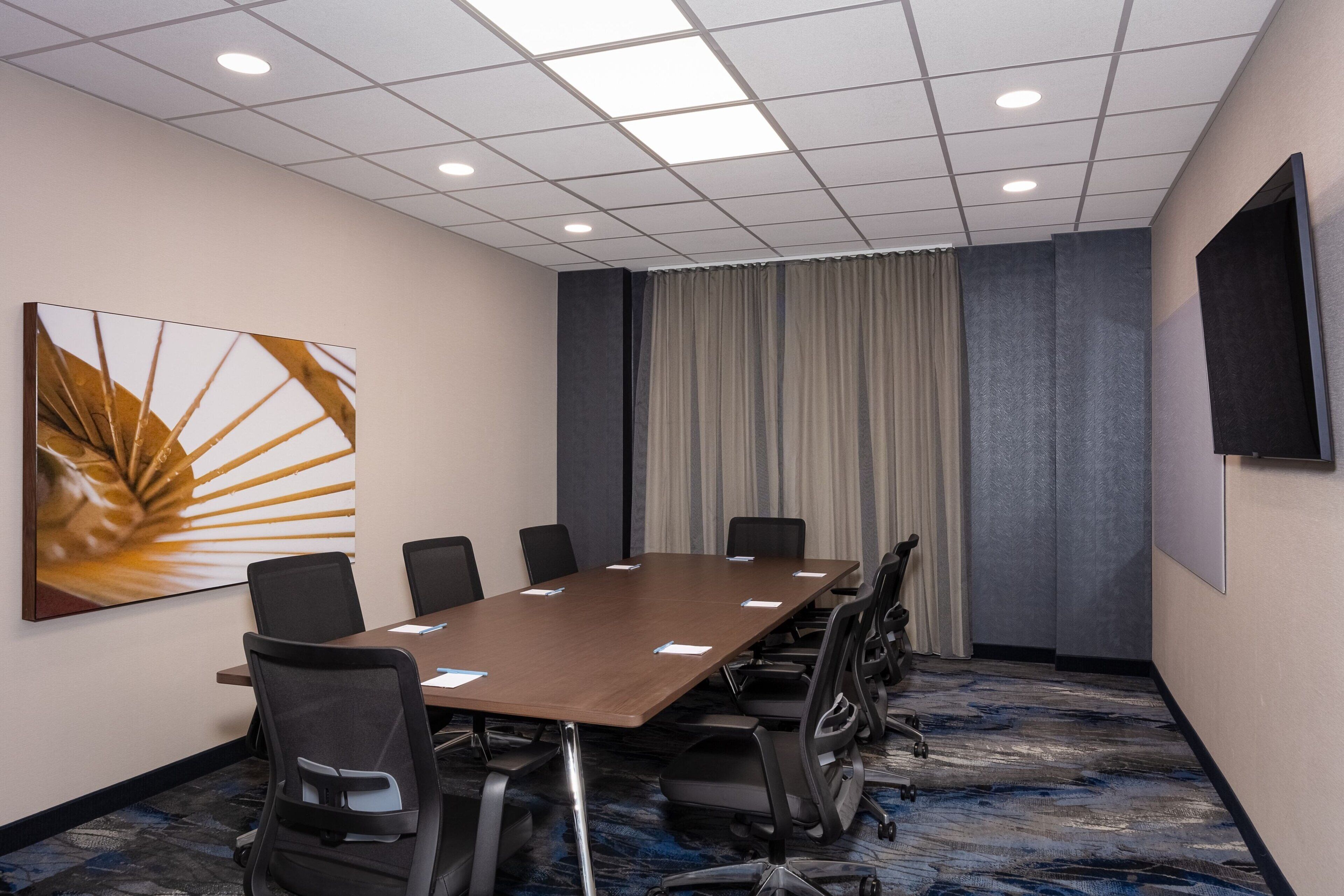 A conference room with a long table, chairs, a large painting, curtains, and a mounted screen.