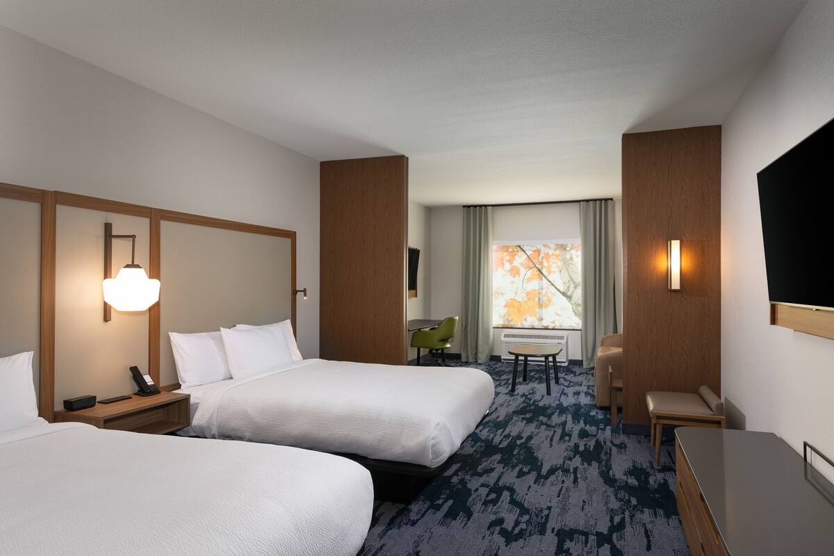 Une chambre d’hôtel avec deux lits, un bureau, une chaise, une télévision et une fenêtre donnant sur un beau paysage.