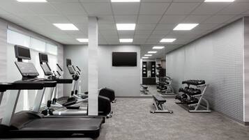 A gym with treadmills, weight machines, and a TV screen.