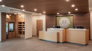 A modern reception area with wooden paneling, a 'Corner Market' sign, and a large decorative wall piece. - Fairfield by Marriott Inn & Suites Omaha at MH Landing (Omaha)