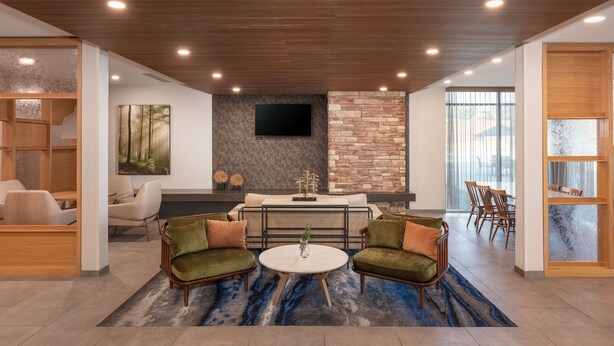 A modern living room with a stone accent wall, a flat-screen TV, and a dining area with wooden furniture. - Fairfield by Marriott Inn & Suites Omaha at MH Landing (Omaha)