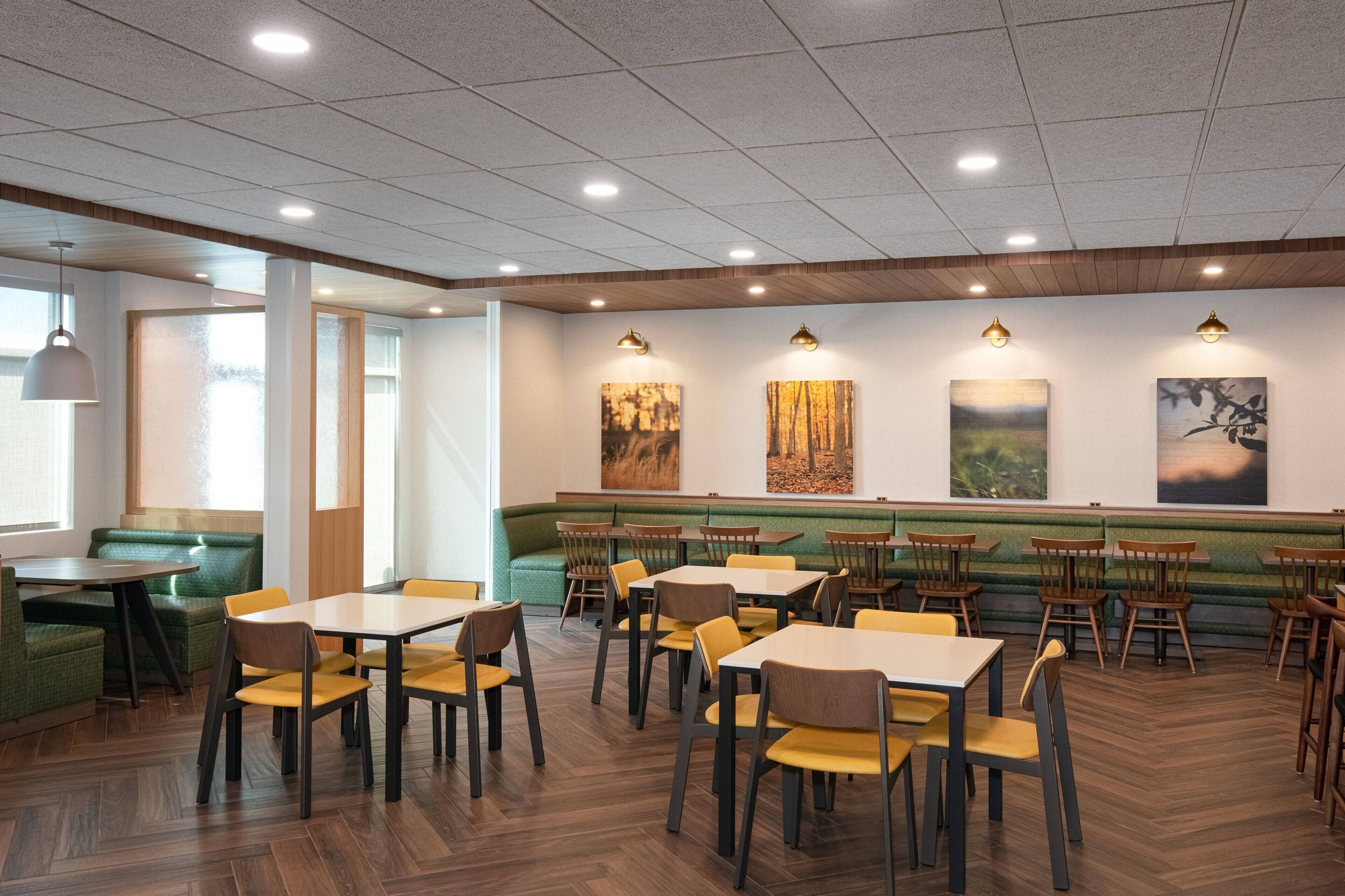 A restaurant with wooden tables and chairs, green cushioned seating, and artwork on the walls.