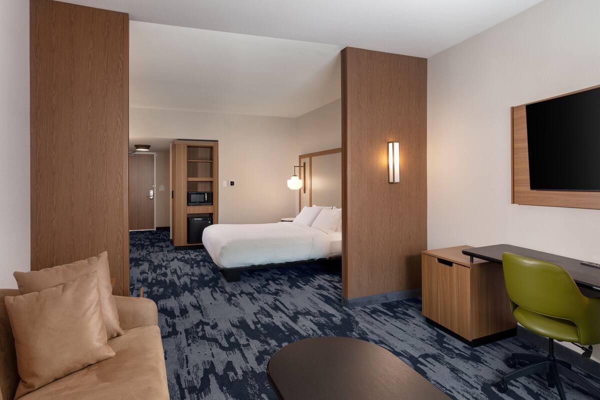 Une chambre d’hôtel avec un lit, un bureau, une chaise verte, un canapé et un téléviseur.