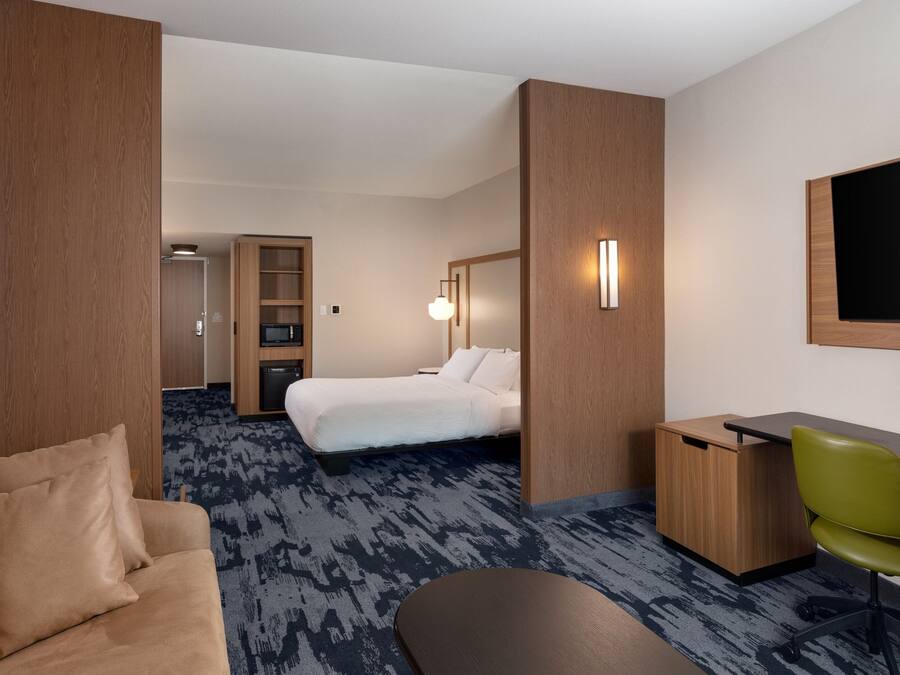 Une chambre d’hôtel avec un lit, un bureau, une chaise verte, un canapé et un téléviseur.