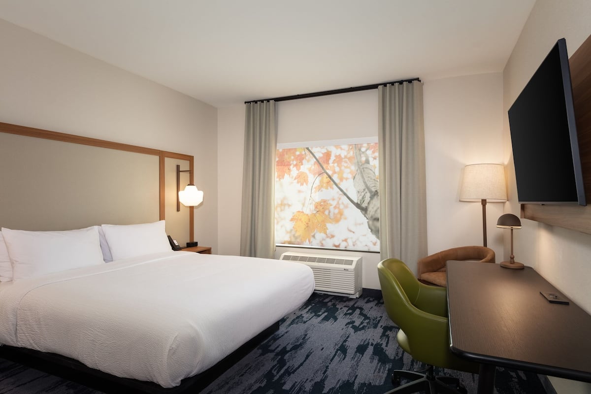 Une chambre d’hôtel avec un grand lit, un bureau, une chaise, une télévision et une fenêtre avec des rideaux.