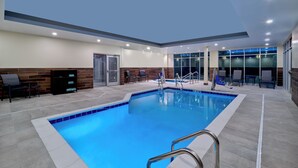 An indoor swimming pool with clear blue water, surrounded by lounge chairs and a seating area with a wooden accent wall. - Fairfield by Marriott Inn & Suites Omaha at MH Landing (Omaha)