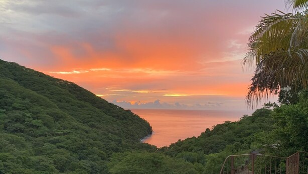 A pool with a view of a sunset over a forested valley.