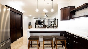 A modern kitchen with a central island, bar stools, dark wood cabinets, and pendant lighting.