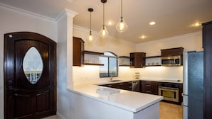 A modern kitchen with a central island, dark wood cabinetry, stainless steel appliances, and pendant lighting.