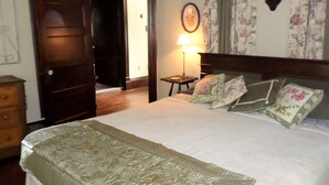A bedroom with a bed, a nightstand, a lamp, a door, and a wall with a floral curtain. - Catskill Classic Charm (Saugerties)