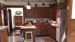 A wooden dining table with a potted fern in the center, a kitchen with wooden cabinets and stainless steel appliances, and a hanging light fixture. - Catskill Classic Charm (Saugerties)
