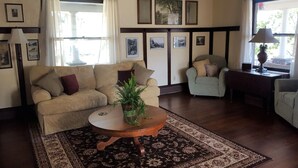 A living room with a beige sofa, a round wooden coffee table with a plant, a patterned rug, and a window with curtains. - Catskill Classic Charm (Saugerties)