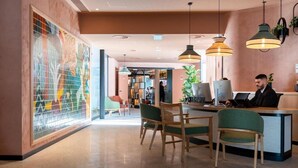 Un vestíbulo de hotel con mostrador de recepción, zona de estar y una gran obra de arte abstracto en la pared.