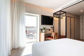A hotel room with a bed, a desk with a chair, a TV mounted on the wall, and a sliding door leading to a balcony. - The Editory Garden Baixa Porto Hotel (Porto)