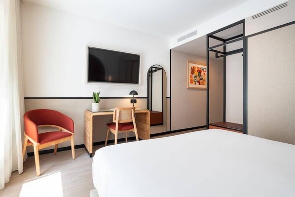 A hotel room with a bed, a desk with two chairs, a TV mounted on the wall, and a painting on the wall. - The Editory Garden Baixa Porto Hotel (Porto)