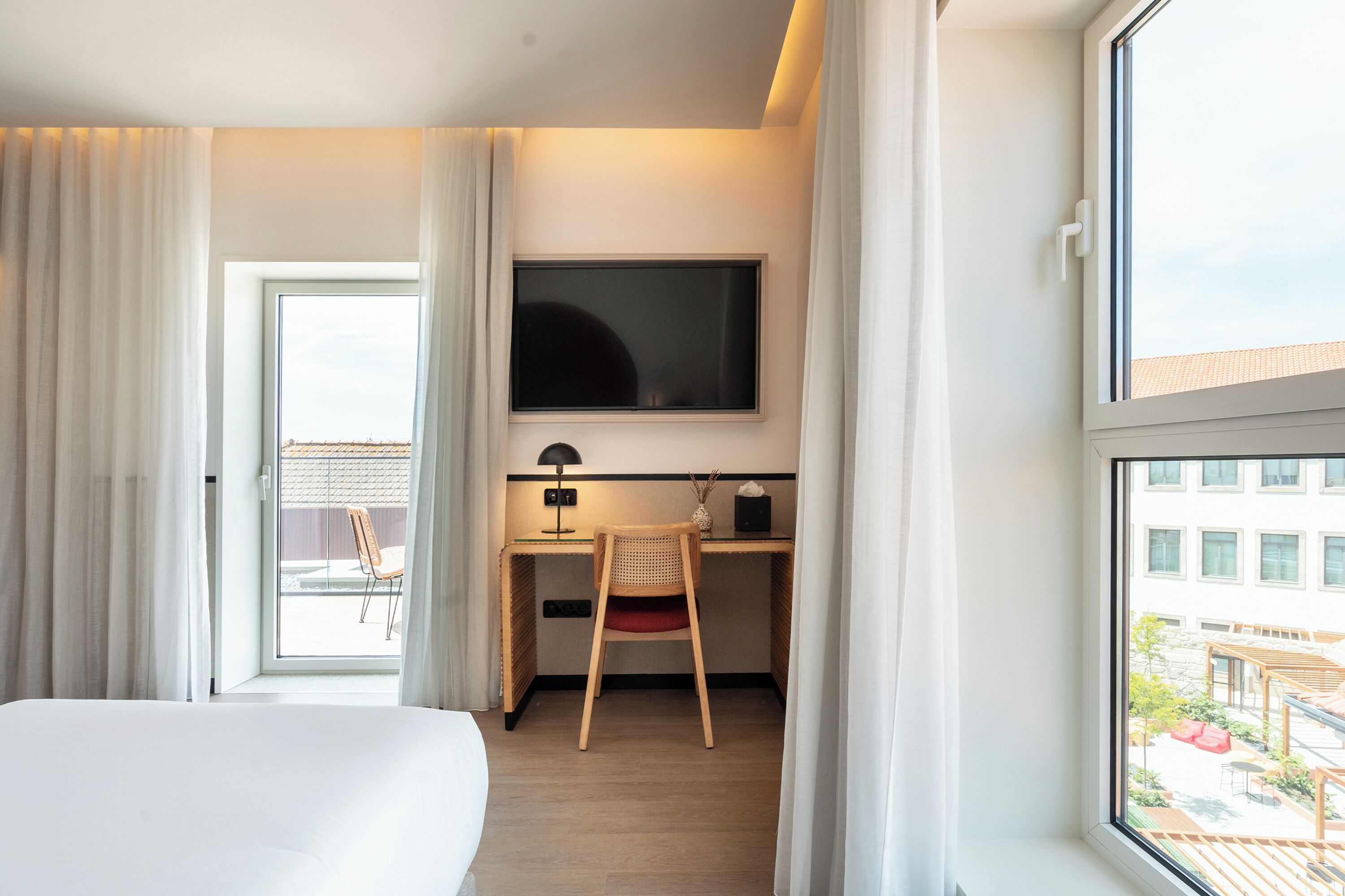 A hotel room with a bed, a desk with a chair, a television, and a window with curtains.