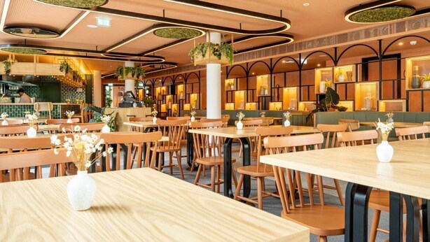Un restaurante con mesas y sillas de madera, una zona de bar y plantas decorativas.