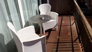 Ein Balkon mit zwei weißen Korbstühlen und einem kleinen runden Tisch.