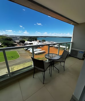 A balcony with a table and chairs, overlooking a marina with boats and a clear blue sky.