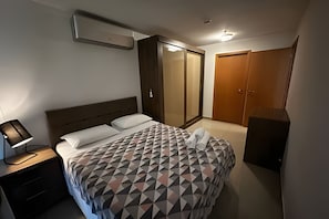 A bedroom with a bed, nightstand, wardrobe, and a mirror.