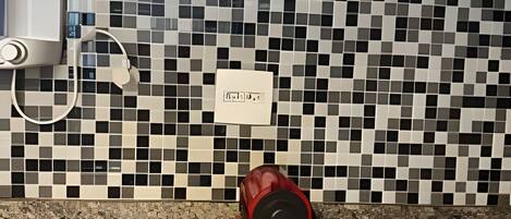 A kitchen with a tiled backsplash, a coffee maker, and a scale on the counter.