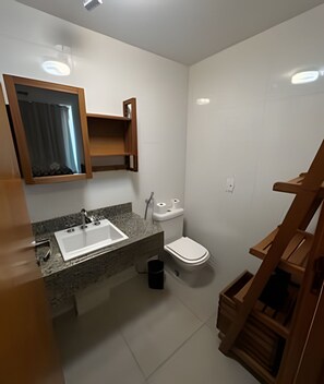 A small bathroom with a sink, toilet, and a wooden shelf.