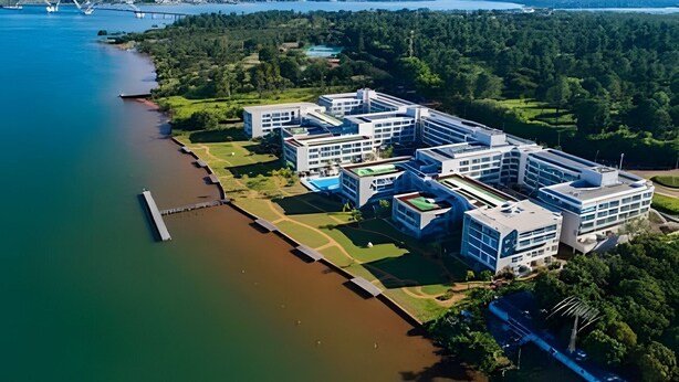 A modern building complex by a river with a bridge in the background. - Brisas do Lago - Apartamento 4 (Brasília)
