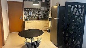 A compact kitchen with a refrigerator, microwave, and a small dining table. - Brisas do Lago - Apartamento 4 (Brasília)
