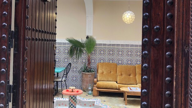 Un interior marroquí con una puerta de madera, un sofá amarillo, un suelo estampado y una planta en maceta.