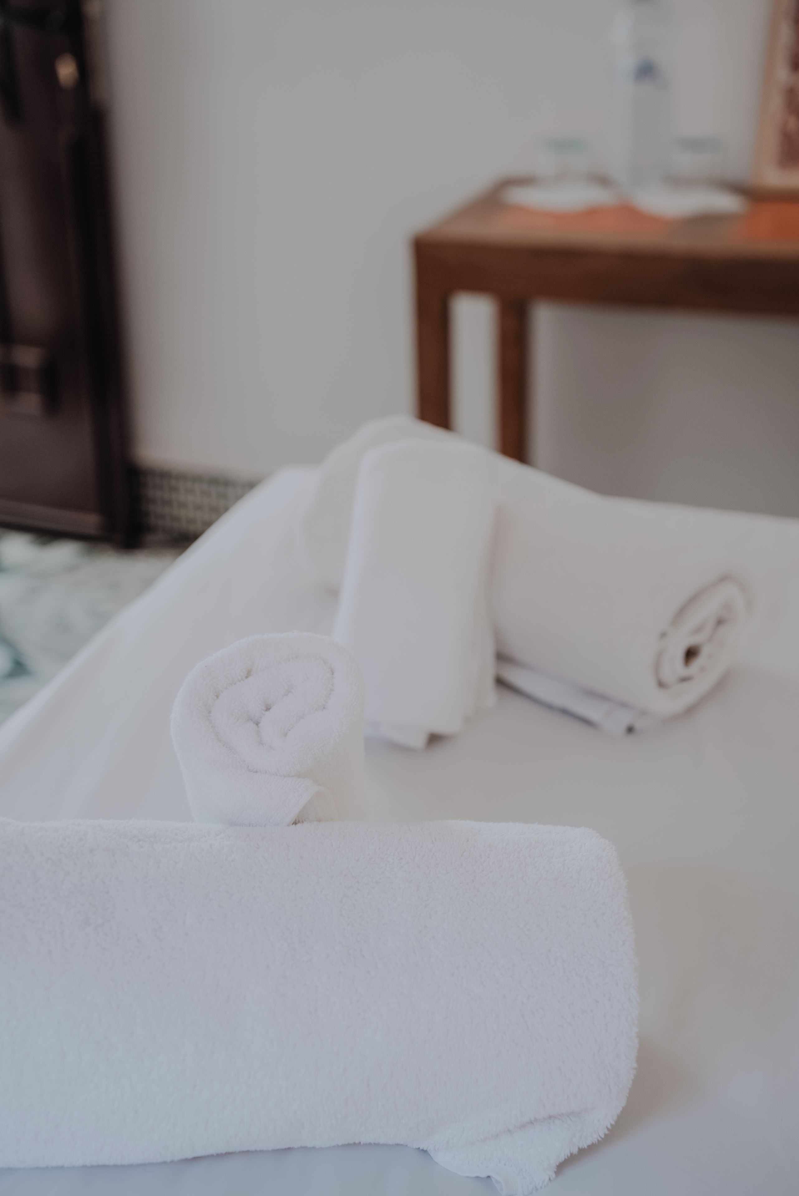 A bed with rolled white towels and a wooden nightstand with a bottle and glasses.