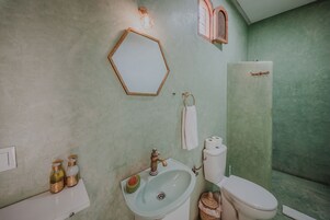Un bagno con lavandino, WC e doccia. C'è uno specchio a parete e un asciugamano appeso.