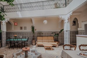 A spacious interior with a high ceiling, a dining area, a seating area with a sofa and ottoman, and a decorative ceiling with a hanging light fixture.